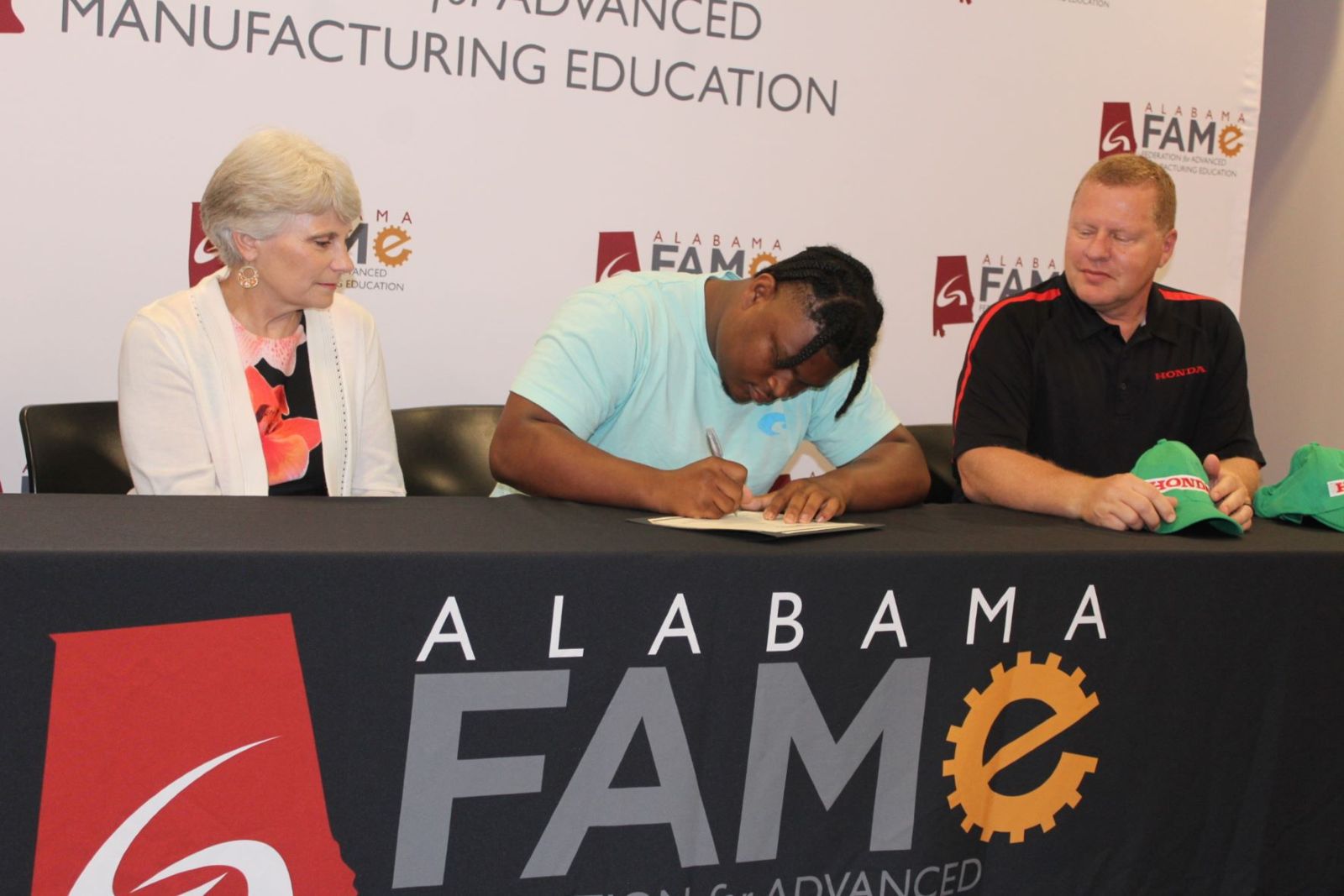 Tyshawn Kerley signs a FAME contract as Dr. Kathy Murphy, president of Gadsden State, and Scott Haywood, technical specialist at Honda of Alabama, look on