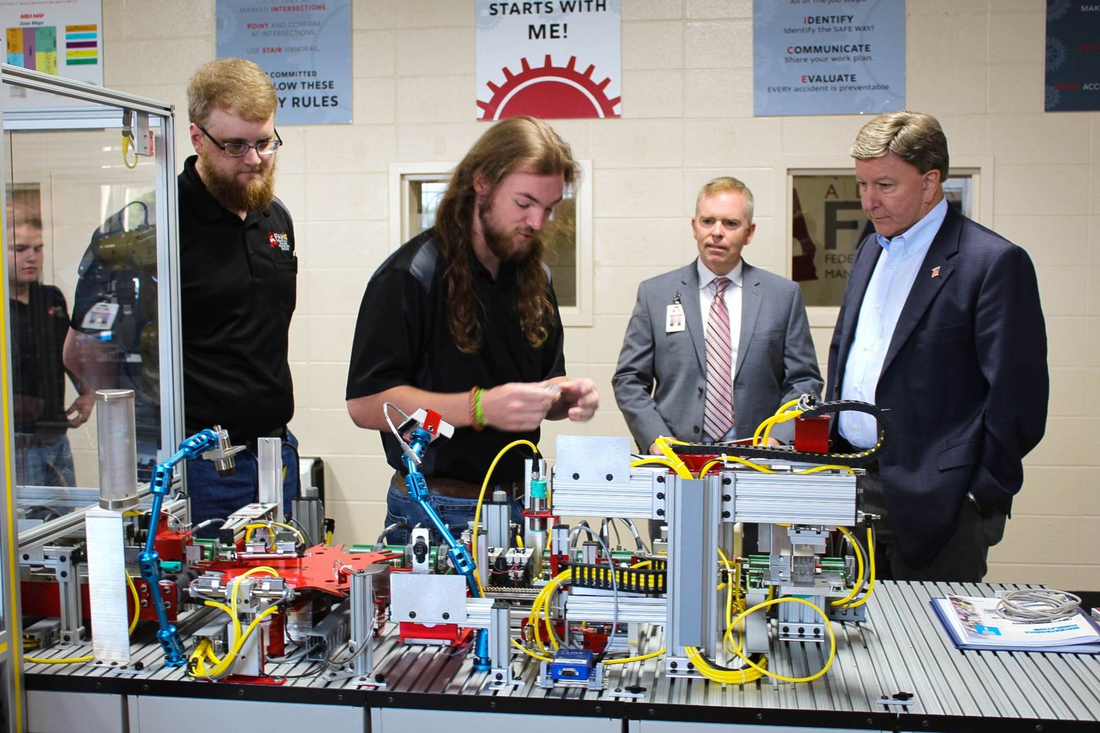 Congressman Mike Rogers takes a tour of the labs at the Advanced Manufacturing Center on the Ayers Campus of Gadsden State Community College. FAME senior students Luke Devin, left, and Wes Simmons explains how the mechantronics line works. They are joined by Alan Smith, second from right, dean of Workforce Development.