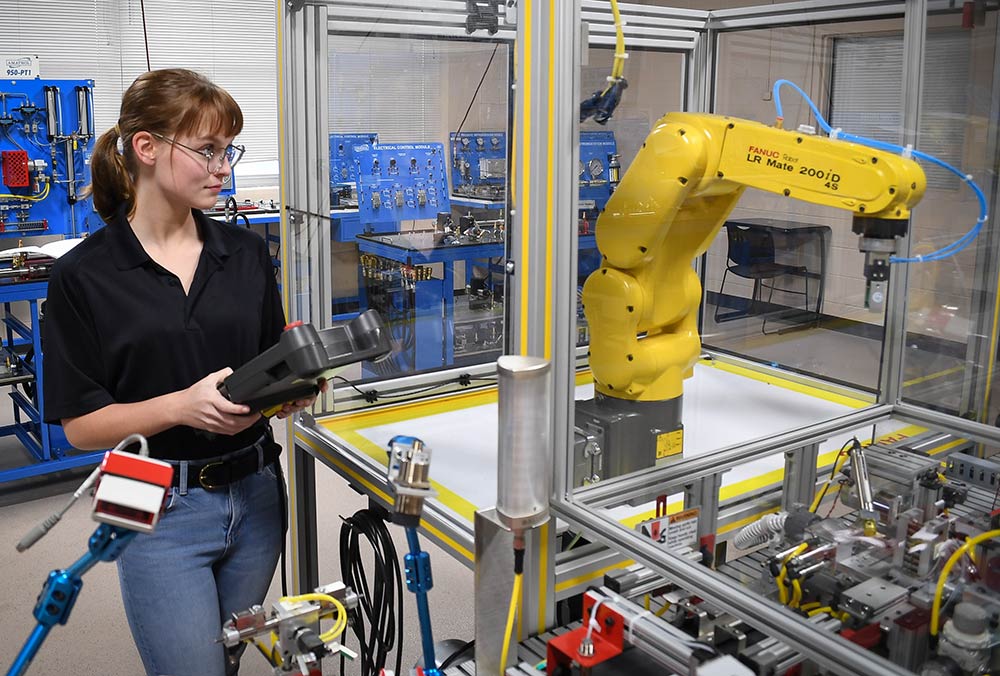 A student operates a robot in the industrial automation classroom on the Ayers campus